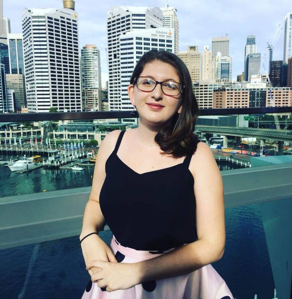 Eva Hopewell, Class of 2016, standing on a balcony overlooking a waterfront marina and city skyline with high-rise buildings in the background