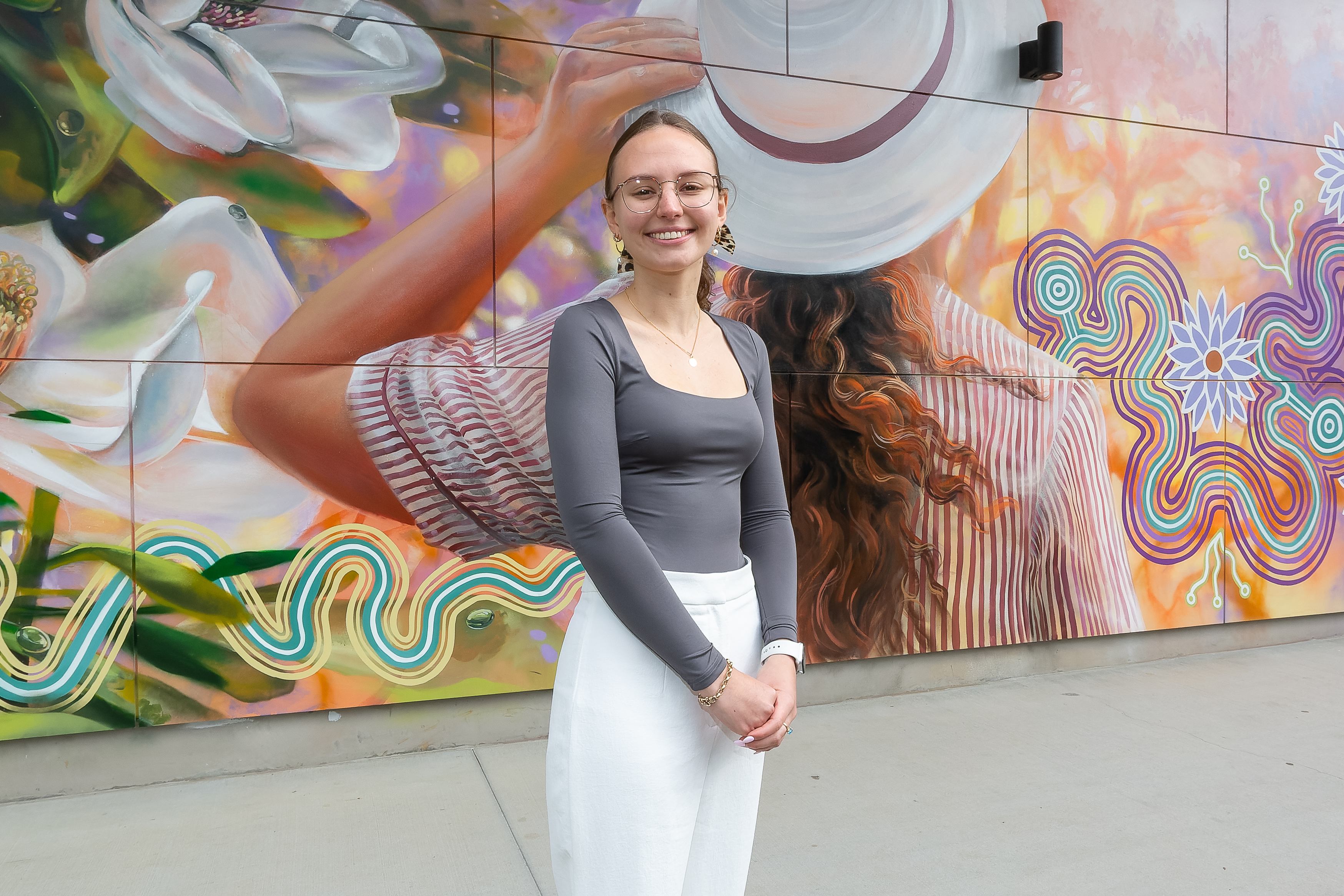 Caitlyn Douglas standing in front of a colourful mural featuring flowing patterns and floral elements