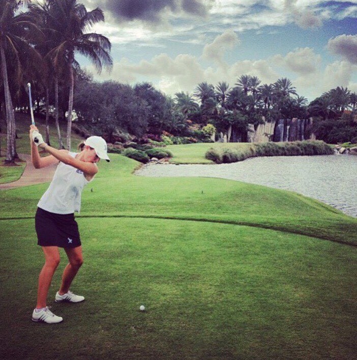 Ellen Chambers playing a golf shot on a lush green course with palm trees and a water feature in the background