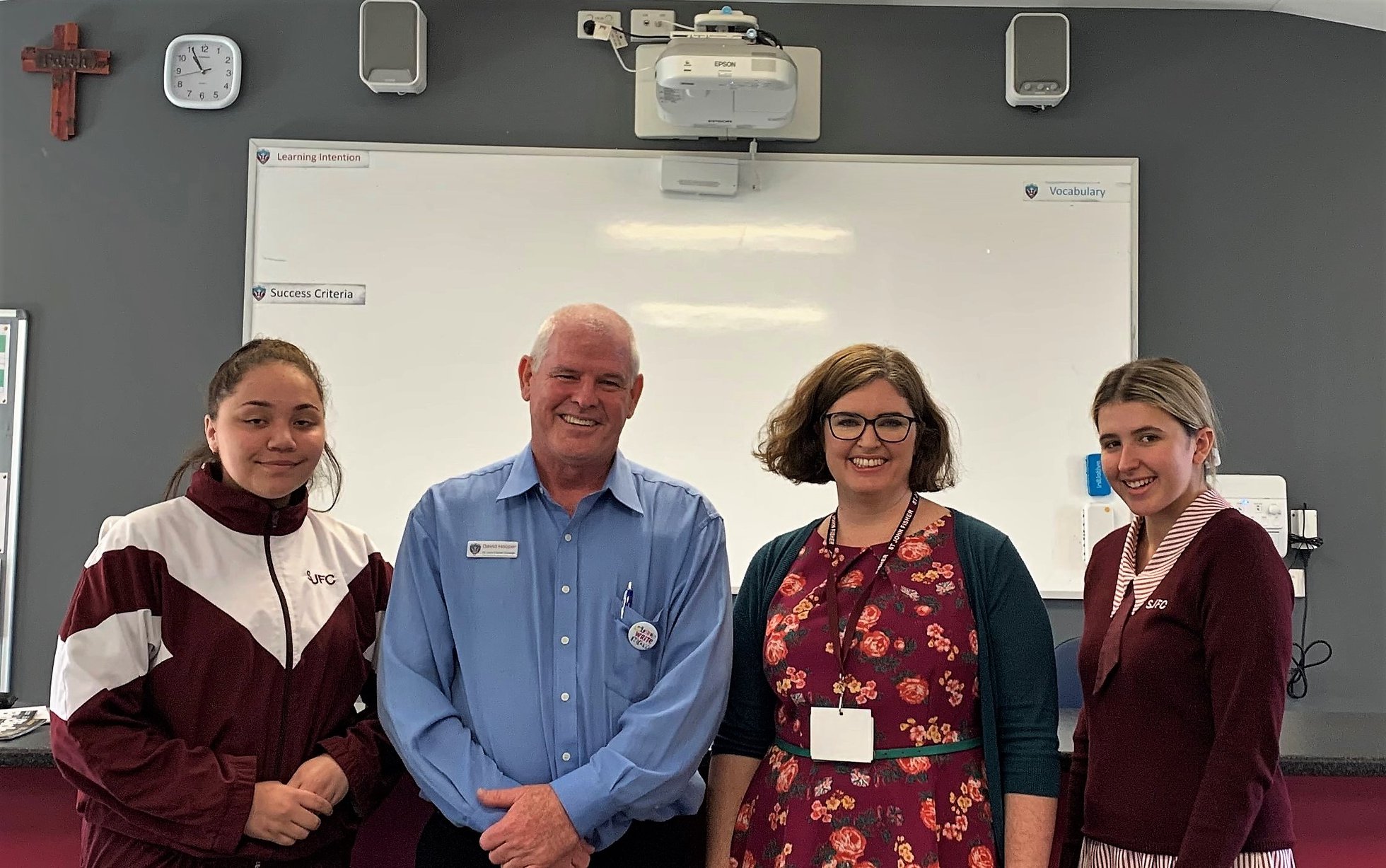 Q&A session with Associate Professor Tracy O’Mara, standing with students in a classroom in front of a whiteboard and learning display